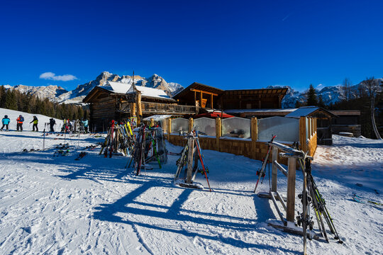 Ski equipment in racks outside a rustic lodge with mountains under a clear blue sky.