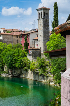 Scenic view of a historic bell tower by a vibrant green river under a blue sky.