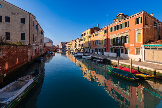 Canal flanked by colorful buildings under a clear blue sky in a quiet urban setting.