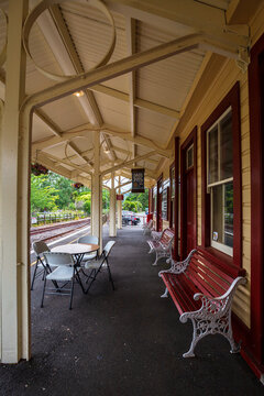 A quiet heritage railway platform in Waikino features red benches, a covered waiting area, and tracks running beside the station