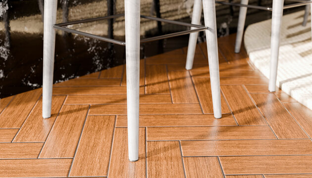 Close-up of chair legs on a herringbone wood floor with sunlight shadows.