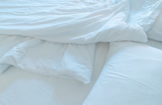 White comfort bed and soft pillow in modern bedroom. White linen blanket in hotel bedroom. Closeup detail of messy white blanket after waking up in morning. Comfortable bed with soft white duvet.