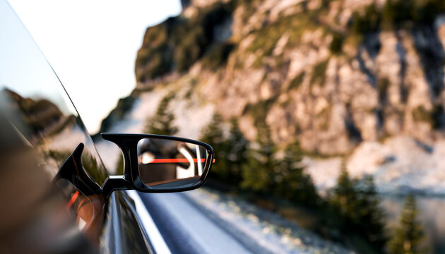 A side mirror reflecting a mountainous road with blurred background and rocky terrain.