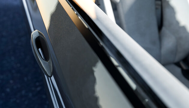 Closeup of a black car's door handle with reflections on a sunny day.