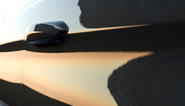 Side view of a car door with reflection of sunset on the surface.
