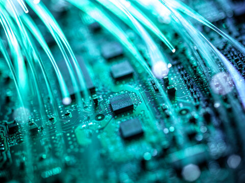 Close-up of a green circuit board with glowing fiber optic strands.