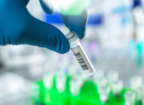 Gloved hand holding a test tube with barcode in a laboratory setting.