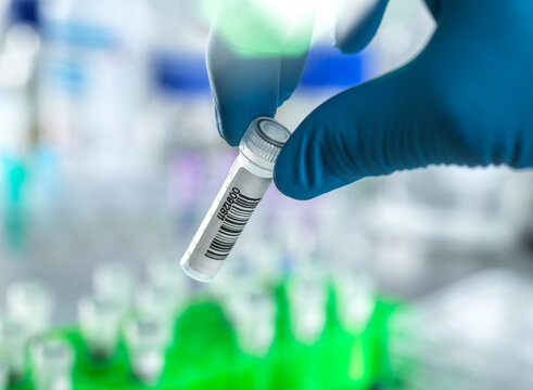Blue-gloved hand holding a small vial with a barcode in a laboratory setting.