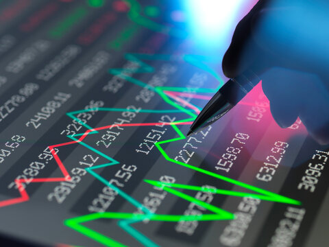 Hand using a stylus on a digital stock market graph display showing rising and falling trends.