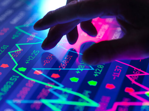 Hand touching a screen displaying a stock market graph with colorful data points.  