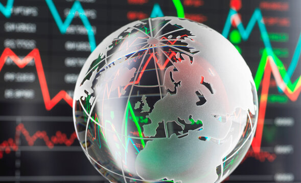 Transparent globe with stock market graphs and data on a screen in the background.