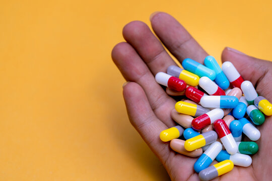 Man hand holding colorful capsule pills on yellow background. Prescription drugs. Drug overuse and polypharmacy concept. Drug allergy. Pharmaceutical industry. Pharmacy banner. Healthcare and medicine