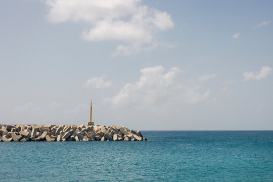 Calm sea with a rocky breakwater and a small lighthouse under a partly cloudy sky. Ly Son island, Vietnam