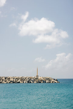 A calm sea and blue sky with fluffy clouds, featuring a breakwater and small lighthouse. Ly Son island, Vietnam