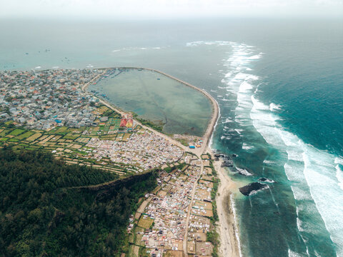 Aerial view of seaside town with buildings, lush greenery, and ocean waves. Ly Son island, Vietnam