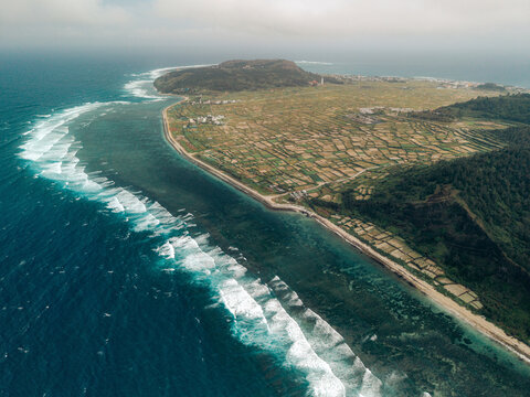 Aerial view of a scenic coastal landscape with waves and lush farmland on a peninsula. Ly Son island, Vietnam