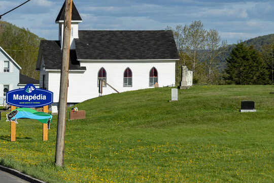Gaspesie, Canada, 30 May 2026 : A white rural church with a steeple stands on a hill next to a cemetery, with a Matapedia welcome sign.