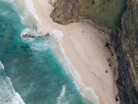 Aerial view of a serene beach with turquoise waves meeting rugged cliffs and white sand. Ly Son island, Vietnam