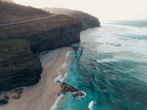 Aerial view of a rugged coastline with cliffs, beach, and turquoise sea under a hazy sky. Ly Son island, Vietnam