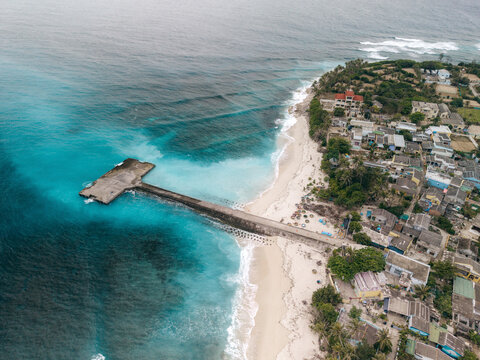 Aerial view of a pier extending into turquoise ocean with beach and lush greenery on the coast. Ly Son island, Vietnam