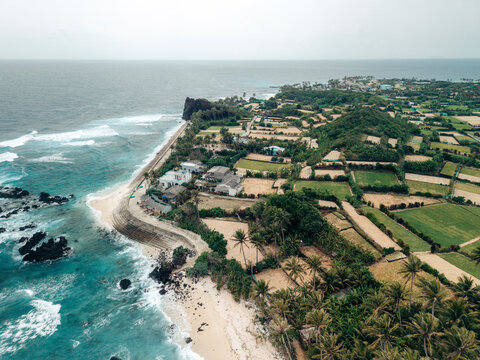 Aerial view of coastal landscape with lush fields and waves crashing on rocky shoreline. Ly Son island, Vietnam