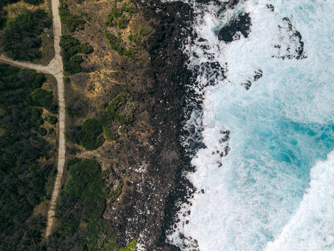 Aerial view of rugged coastline with crashing waves and rocky landscape meeting green vegetation. Ly Son island, Vietnam