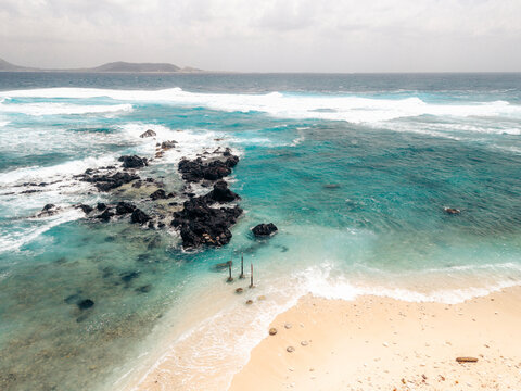 Stunning aerial view of turquoise ocean waves crashing against rocks on a sandy beach. Ly Son island, Vietnam