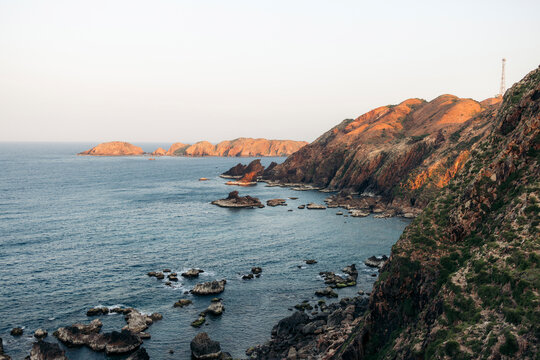 Rocky coastline at sunset with rugged cliffs and calm ocean waves in a serene landscape.