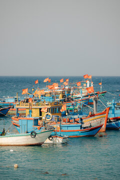 Colorful fishing boats with red flags float on a calm sea under a clear sky.