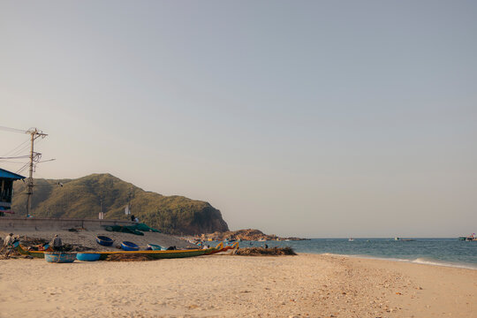 Sandy beach with scattered boats and distant hills under a clear sky