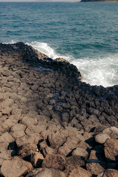 Interlocking hexagonal basalt columns meet ocean waves under a clear blue sky.
