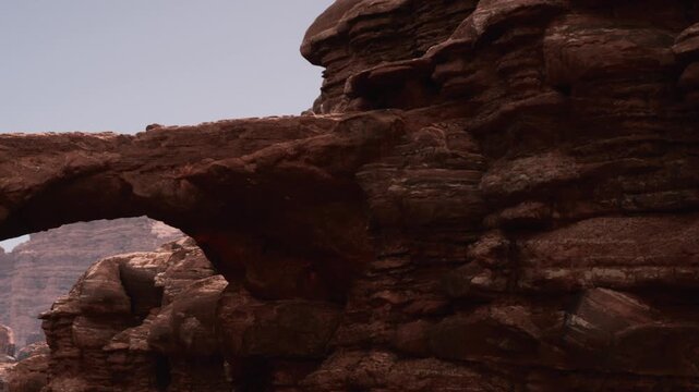 Visitors explore a large rock arch surrounded by rugged rock formations in the desert. Sunlight highlights the textures of the rocks during the day.