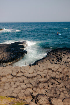 Rocky hexagonal basalt formations meet the ocean under a clear blue sky.  