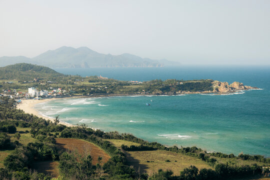 Coastal landscape with green hills, sandy beaches, blue sea, and distant mountains.