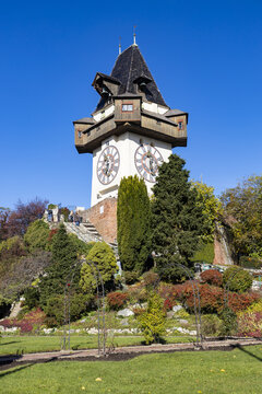 View of the historic Graz Clock Tower with its large clock faces and wooden balconies on the Schlossberg hill under a clear blue sky in Graz, Styria, Austria.