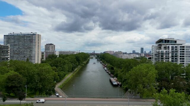 Aerial view of the Brussels-Charleroi Canal with a bridge, apartment blocks, and lush green trees under a cloudy sky in Anderlecht, Brussels, Belgium.