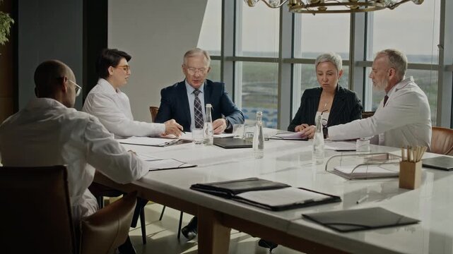 Long shot of diverse partners and scientists in lab coats discussing papers during oil industry meeting, senior businessman standing to shake hands with Indian colleague. Ideal for corporate use