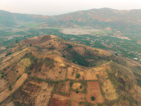 An aerial view of patchwork farmland on a hilly landscape under a hazy sky.