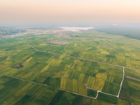Aerial view of vast patchwork fields with winding roads and distant horizon at sunset.