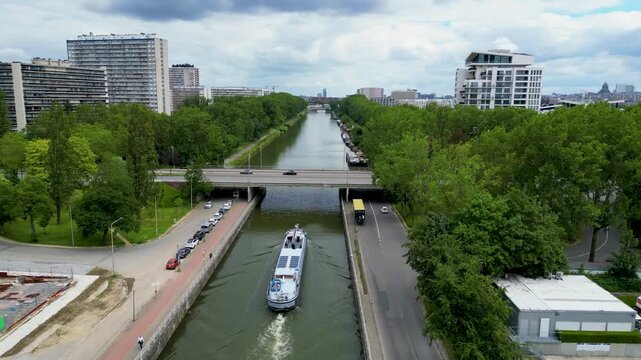 Aerial view of a large barge navigating a canal under a road bridge surrounded by trees and buildings Anderlecht, Brussels, Belgium.