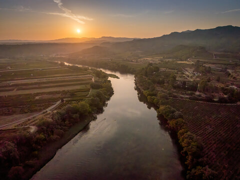 Aerial view of a river meandering through valley hills at sunset with a warm sky.