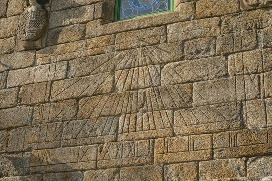 Ancient stone wall with a carved sundial and Roman numerals in sunlight.
