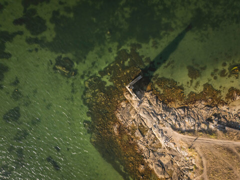 Aerial view of a rocky coastline with a path leading into the green sea.