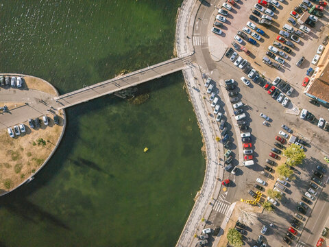 Aerial view of a bridge over a green river with parked cars on both sides.