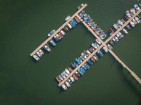 Aerial view of marina with rows of boats docked on green water.