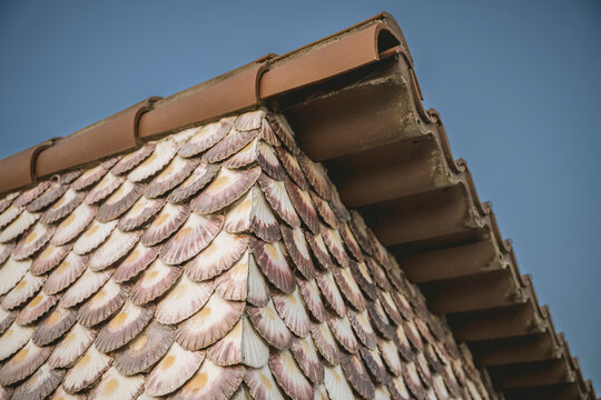 Close-up of a building corner with textured scalloped tiles under a clear blue sky.