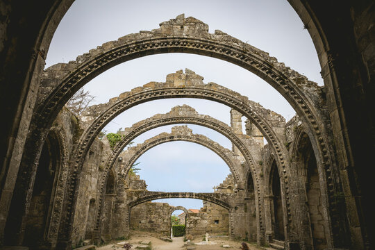 Ancient stone arches of a historic ruin under a cloudy sky, showcasing intricate architecture.