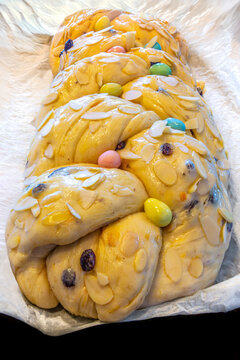 Braided sweet bread with almonds and colorful candy eggs on parchment paper.