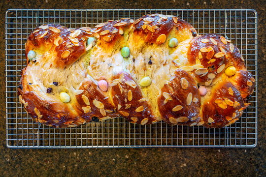 Loaf of braided sweet bread with colorful candies and almond slices on a cooling rack.