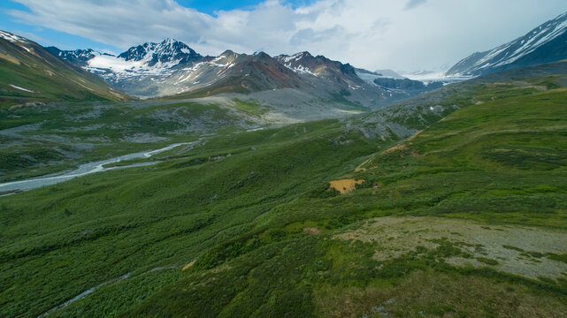 Verdant mountain landscape with rivers and snow-capped peaks under partly cloudy skies. Isabel Pass, Alaska, USA